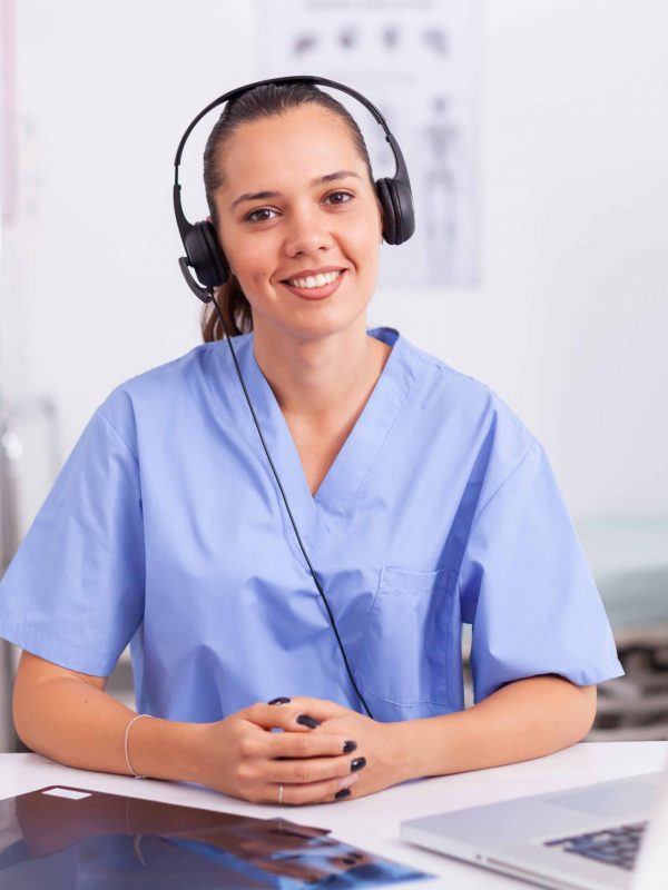 Young practitioner doctor working at the clinic reception desk talking with patients wearing headphones. Female nurse, doctor having a conversation with sick person during consultation, medicine.